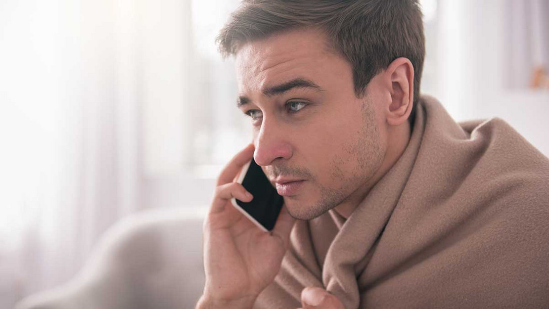 Mann mit Decke um den Hals telefoniert mit einem Handy. 