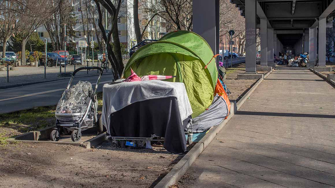 Ein Zelt steht in einer Großstadt unter einer Bahnbrücke. 