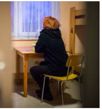 Frau von hinten zu sehen sitzt am Tisch vor einem Fenster