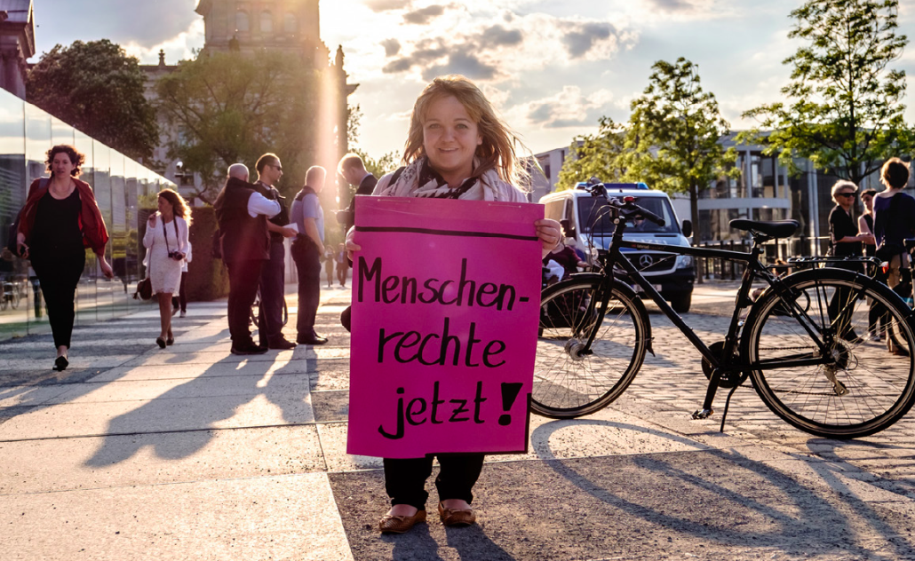 Frau mit einem Plakat und der Forderung: Menschenrechte jetzt!