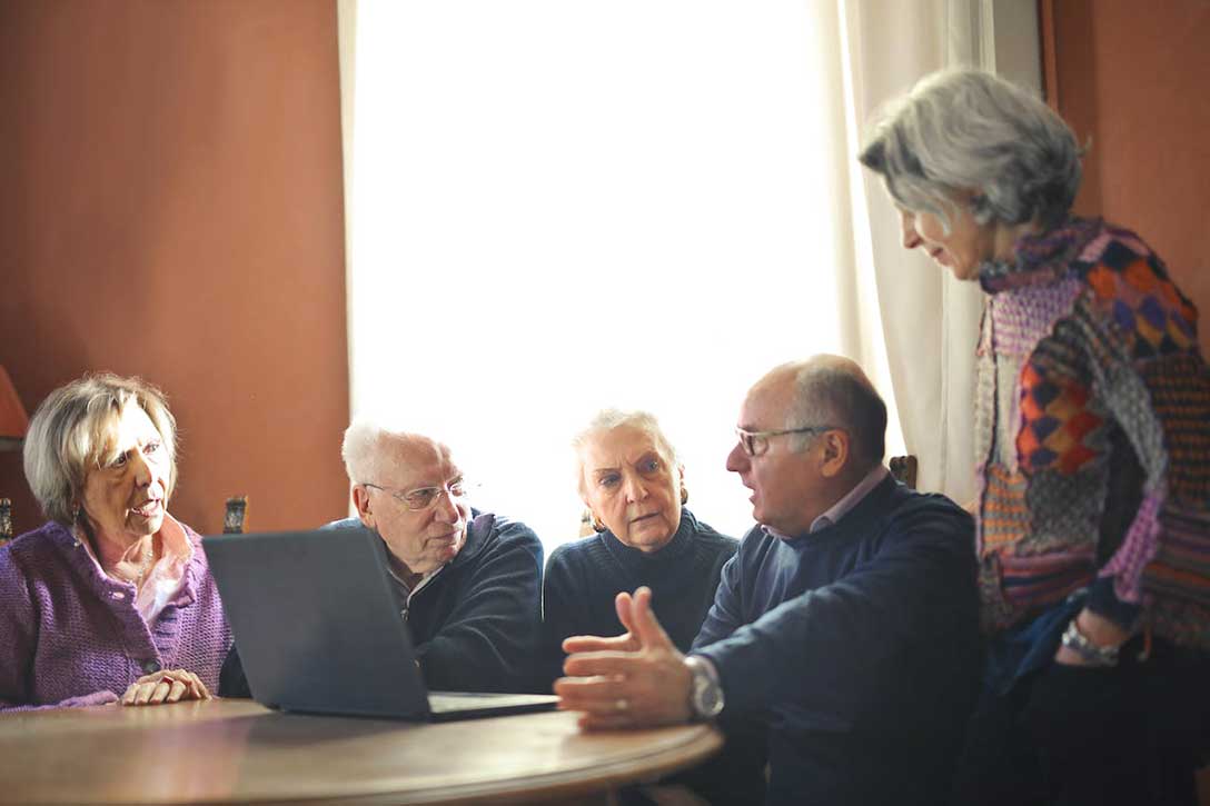Gruppe älterer Menschen sitzt an einem Tisch und diskutiert. 
